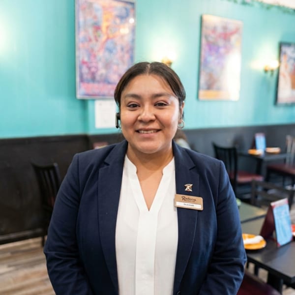 Smiling woman in a navy blazer and white shirt with a name tag in a restaurant.