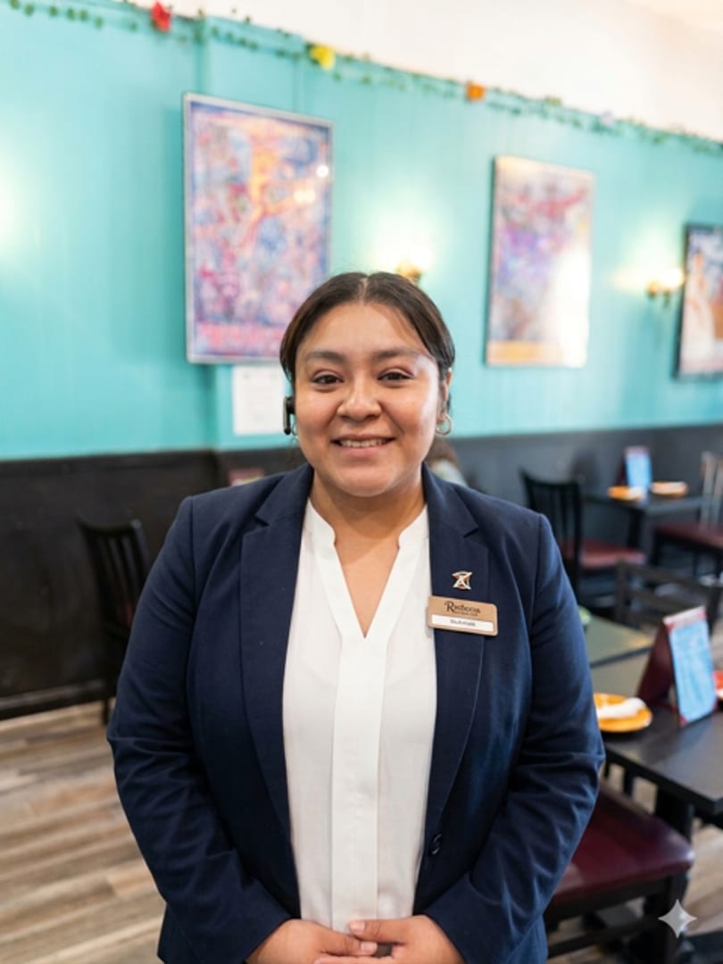 Smiling woman in a navy blazer and white shirt with a name tag in a restaurant.